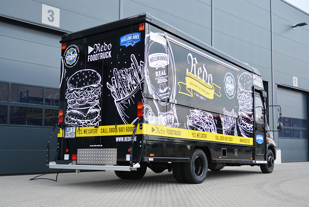 Schwarzer Food Truck mit aufwendiger Fahrzeugbeschriftung.